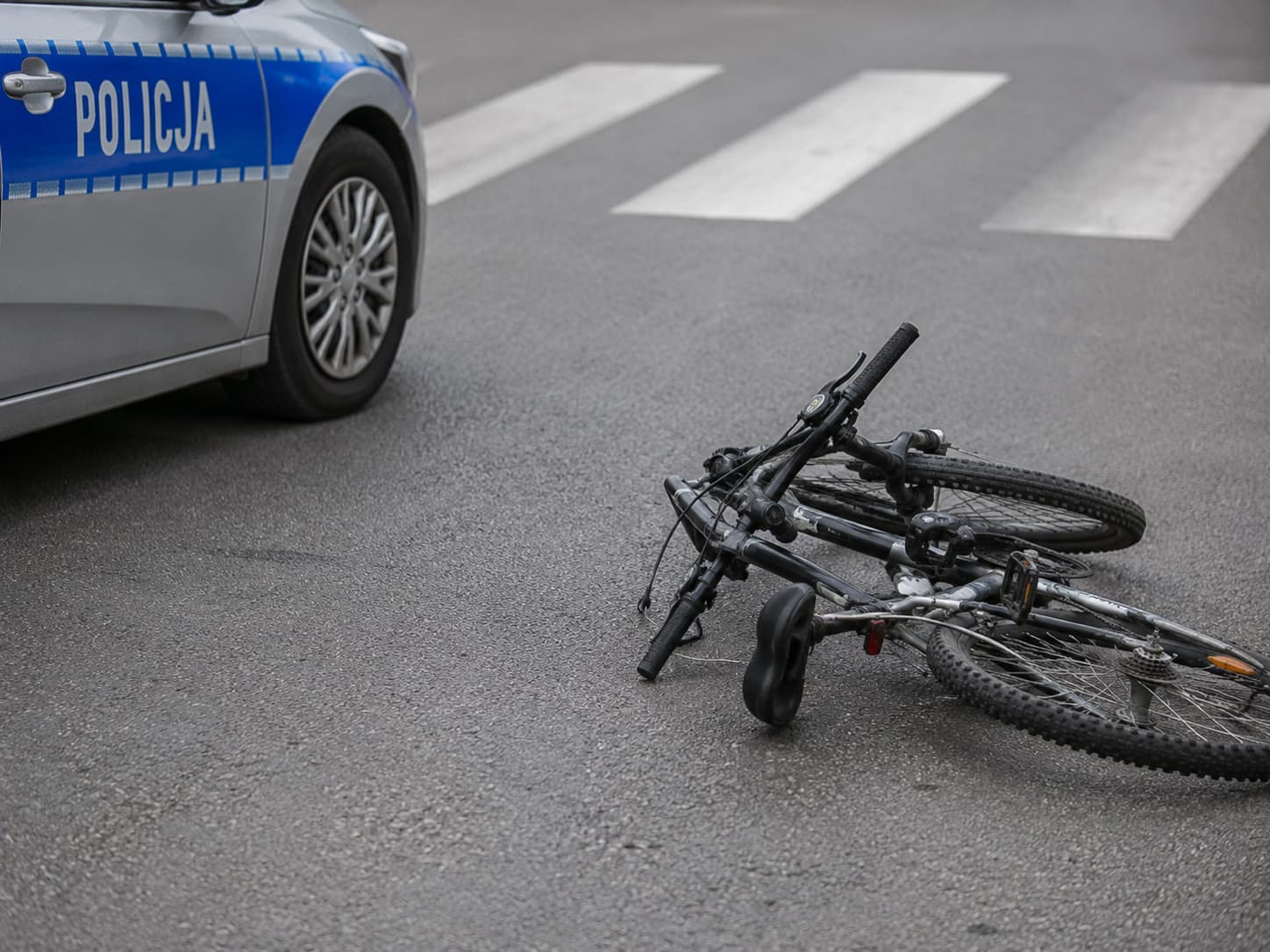 Ilustracja AI przedstawiająca przewrócony rower obok radiowozu policji na jezdni