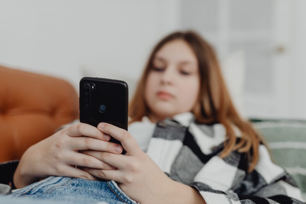 Dziewczynka korzystająca z telefonu jako ilustracja tekstu o socjoterapii dzieci i młodzieży