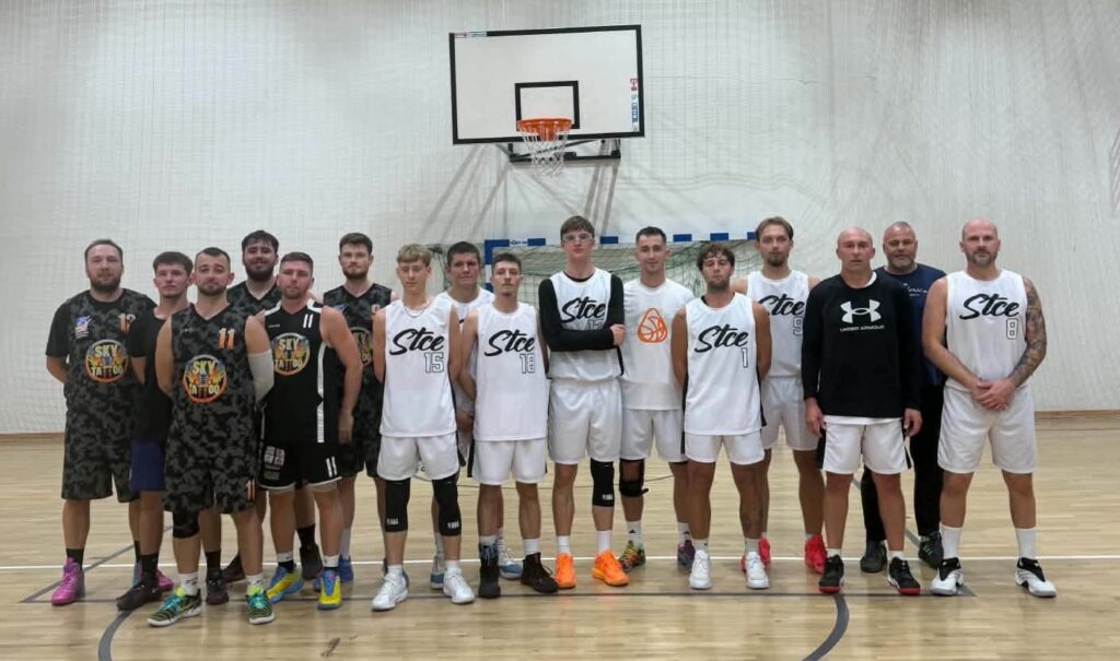 Grupa koszykarzy w strojach sportowych pozująca pod koszem w hali