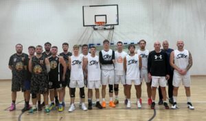 Grupa koszykarzy w strojach sportowych pozująca pod koszem w hali